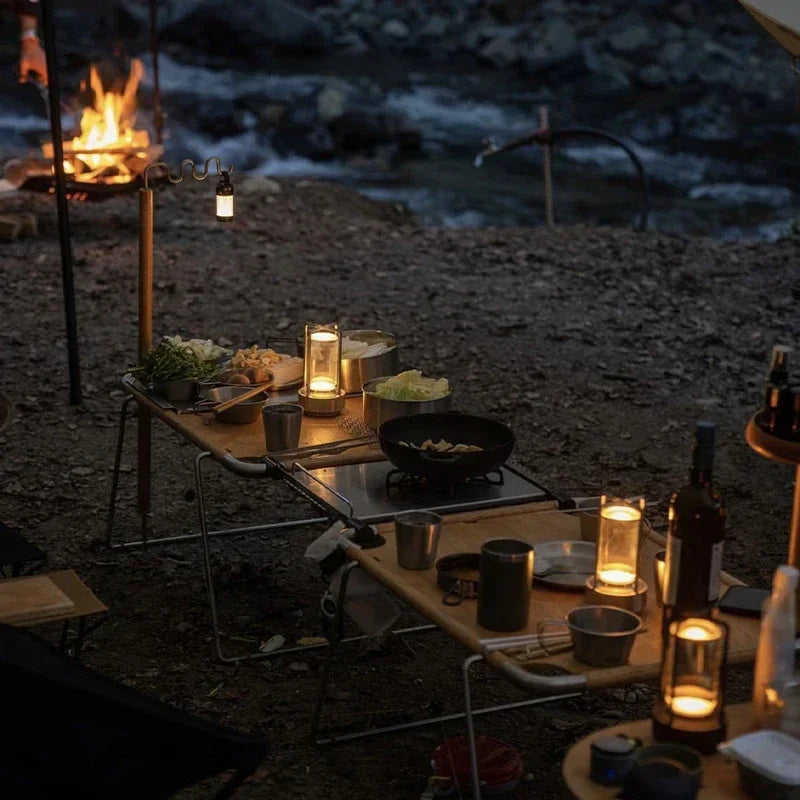 Camping scene with a table by a fire near a body of water at night.