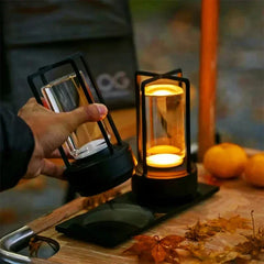 Hand holding a black lantern with a lit candle on a wooden surface 