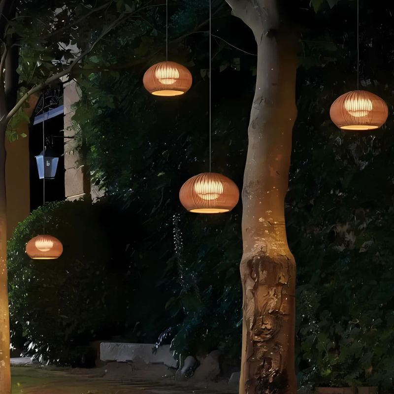 Decorative hanging lights in a garden setting with trees and a building in the background.