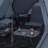 Camping scene with a table by a fire near a body of water at night.